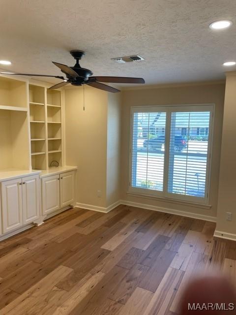 empty room featuring ceiling fan, built in features, a textured ceiling, and light hardwood / wood-style flooring