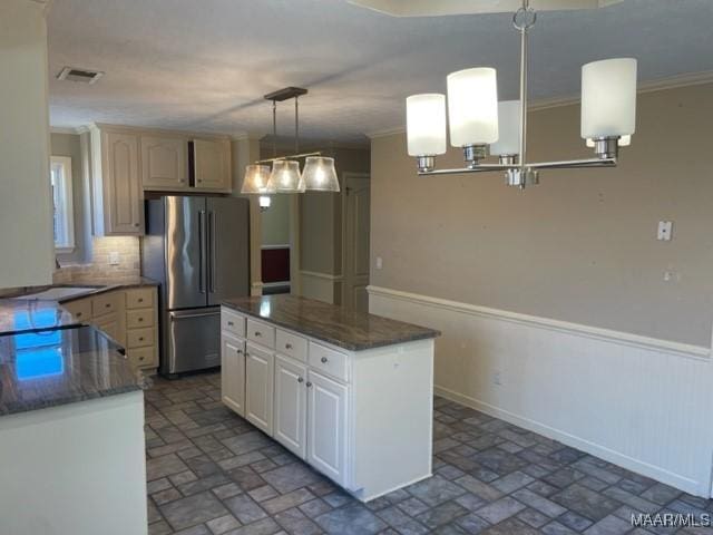 kitchen with white cabinets, crown molding, decorative light fixtures, a kitchen island, and stainless steel refrigerator