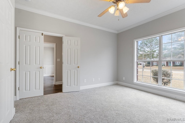 carpeted empty room featuring a healthy amount of sunlight, ceiling fan, and ornamental molding