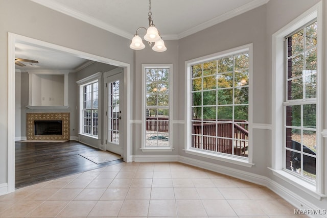 unfurnished dining area featuring light tile patterned floors, ceiling fan with notable chandelier, crown molding, and a tiled fireplace