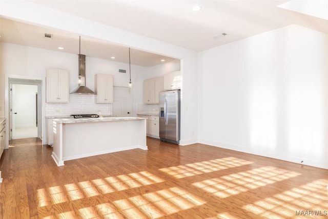 kitchen with pendant lighting, stainless steel fridge with ice dispenser, wall chimney exhaust hood, a kitchen island, and white cabinetry