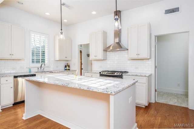 kitchen with a center island, white cabinets, wall chimney range hood, and appliances with stainless steel finishes