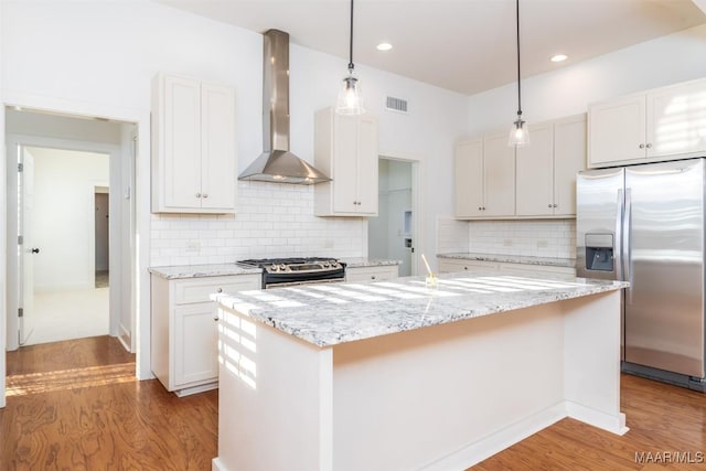 kitchen with stainless steel appliances, white cabinetry, a kitchen island with sink, and wall chimney range hood