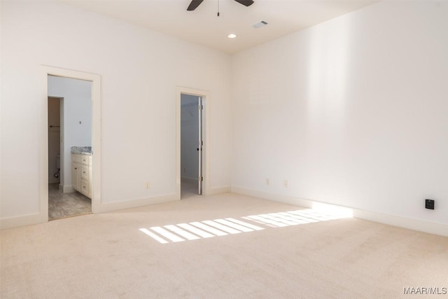 unfurnished bedroom with light colored carpet, ensuite bath, a spacious closet, and ceiling fan