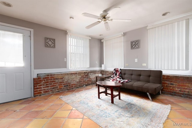 living room with ceiling fan, light tile patterned floors, and brick wall