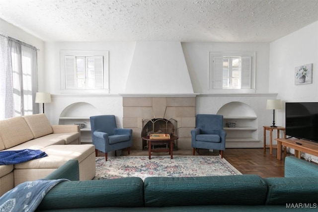 living room with dark parquet flooring, a textured ceiling, built in features, and a tiled fireplace