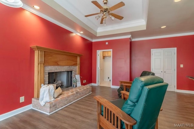 living room with hardwood / wood-style floors, ceiling fan, crown molding, and a brick fireplace