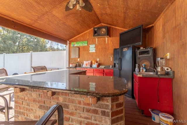 kitchen with lofted ceiling, wood walls, black fridge with ice dispenser, and wooden ceiling