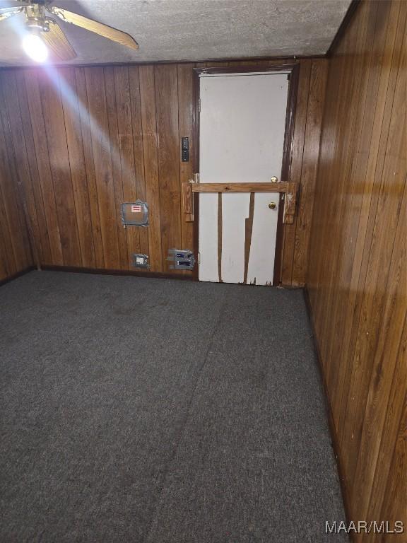 unfurnished room featuring carpet floors, wood walls, ceiling fan, and a textured ceiling