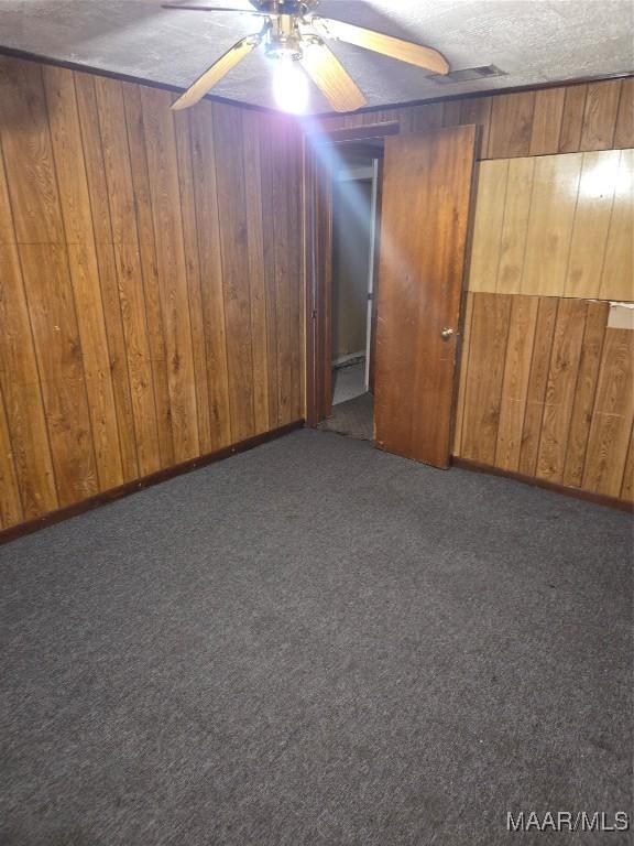 basement featuring ceiling fan, wood walls, a textured ceiling, and dark carpet