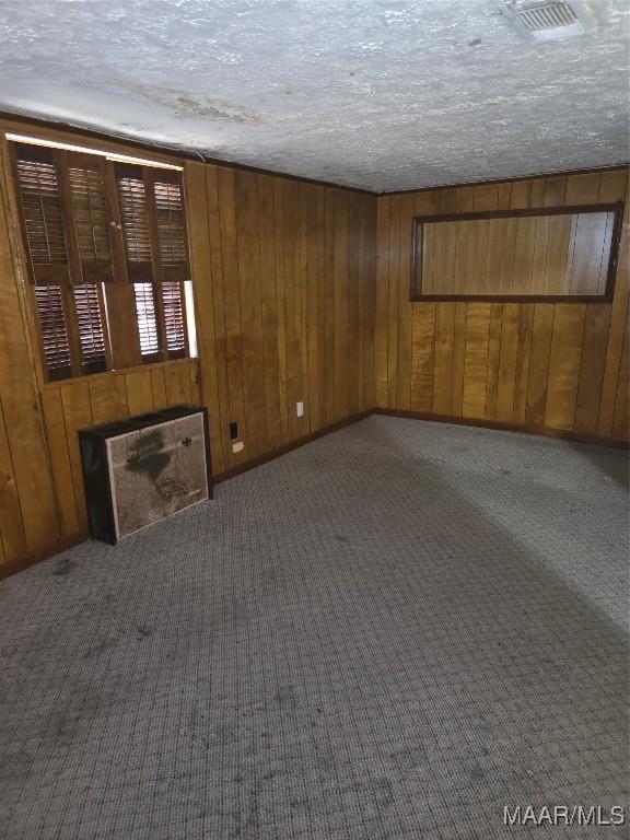 unfurnished living room with carpet flooring, a textured ceiling, and wooden walls