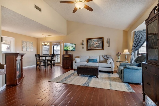 living room with ceiling fan with notable chandelier, dark hardwood / wood-style flooring, lofted ceiling, and a textured ceiling