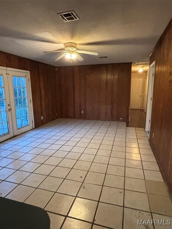 tiled empty room featuring french doors, a textured ceiling, ceiling fan, and wooden walls