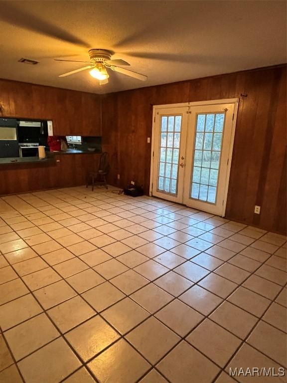 unfurnished living room with ceiling fan, light tile patterned flooring, wooden walls, and french doors