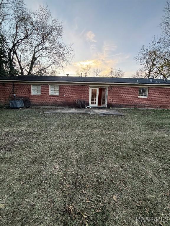 back house at dusk featuring a lawn and central air condition unit