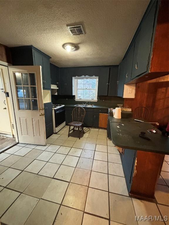 kitchen featuring light tile patterned floors, a textured ceiling, white range with gas cooktop, and sink