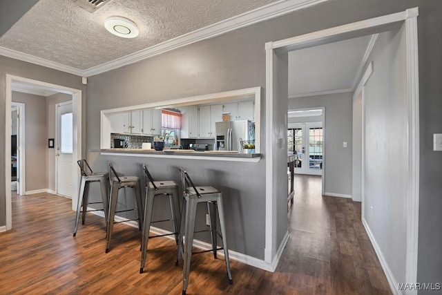 interior space featuring decorative backsplash, stainless steel fridge, a textured ceiling, crown molding, and white cabinets