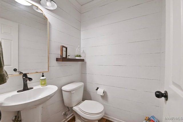 bathroom featuring wood walls, toilet, and sink