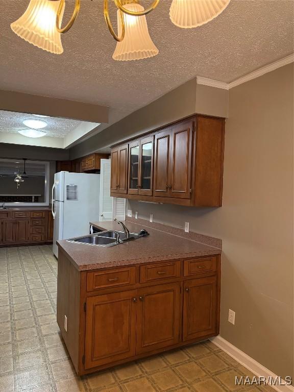 kitchen featuring a textured ceiling, white refrigerator, crown molding, and sink