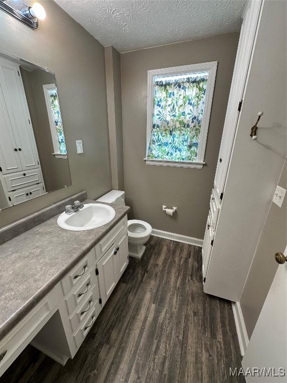 bathroom with a textured ceiling, hardwood / wood-style flooring, toilet, and a wealth of natural light