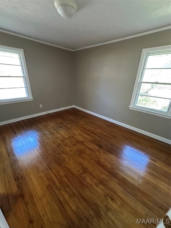 empty room with dark hardwood / wood-style flooring and crown molding