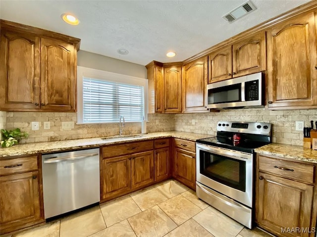 kitchen featuring sink, light stone countertops, light tile patterned floors, tasteful backsplash, and stainless steel appliances