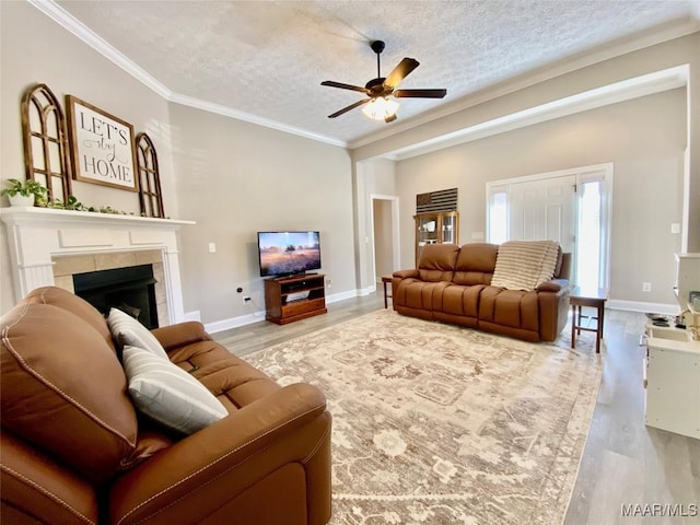 living room featuring light wood-type flooring, a textured ceiling, ceiling fan, crown molding, and a fireplace