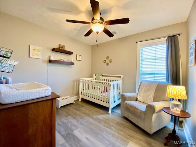 bedroom with a crib, hardwood / wood-style floors, and ceiling fan