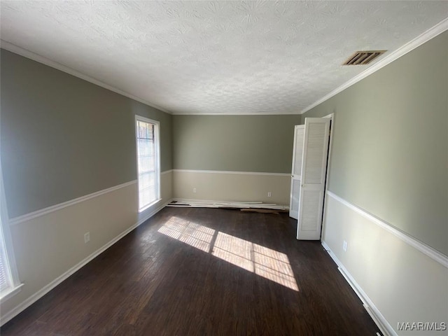 empty room featuring a textured ceiling, crown molding, and dark wood-type flooring