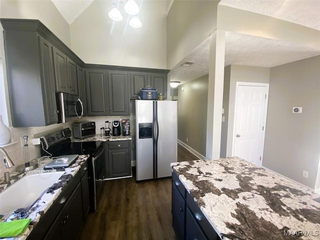 kitchen featuring light stone countertops, appliances with stainless steel finishes, a textured ceiling, dark wood-type flooring, and sink