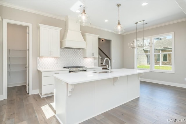 kitchen featuring gas stove, white cabinetry, sink, premium range hood, and an island with sink