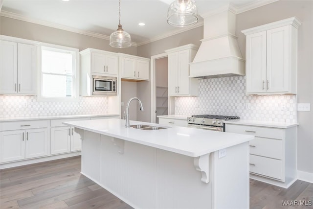 kitchen featuring appliances with stainless steel finishes, custom range hood, sink, decorative light fixtures, and an island with sink