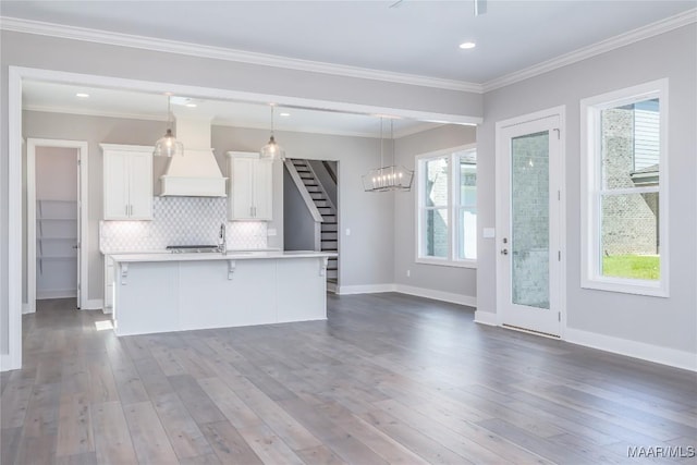 kitchen with custom exhaust hood, an island with sink, tasteful backsplash, decorative light fixtures, and white cabinetry