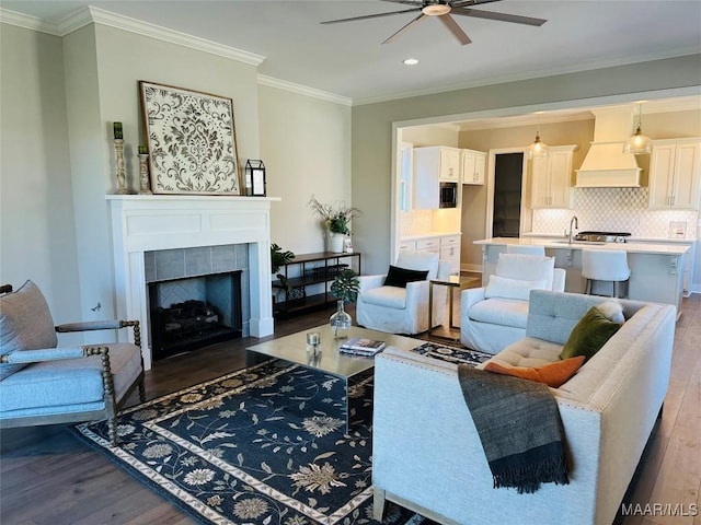 living room featuring ceiling fan, sink, dark hardwood / wood-style flooring, a tiled fireplace, and ornamental molding