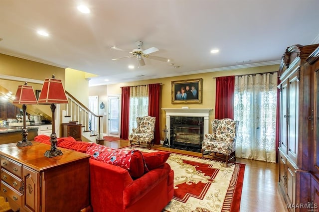 living room featuring ceiling fan, light hardwood / wood-style floors, ornamental molding, and a high end fireplace