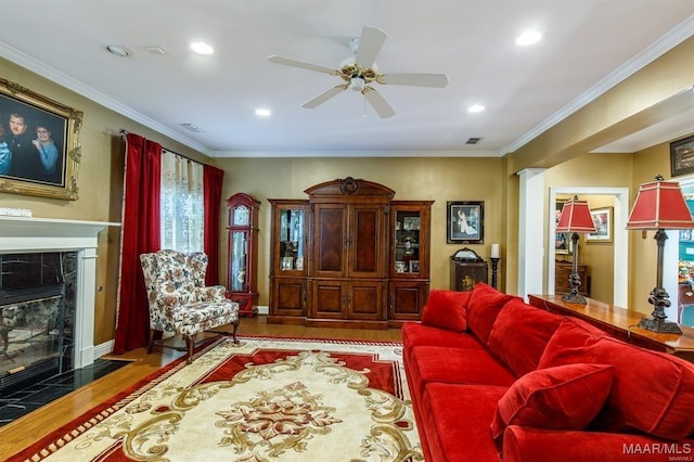 living room featuring hardwood / wood-style flooring, ceiling fan, crown molding, and a tiled fireplace