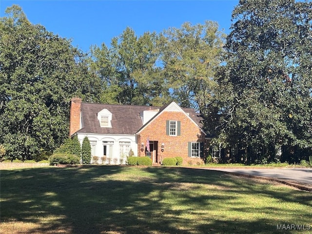 cape cod-style house featuring brick siding, a chimney, and a front yard