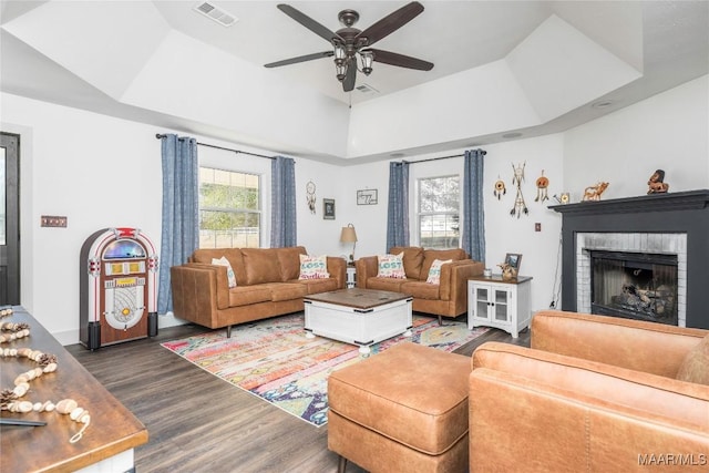 living room with a tray ceiling, ceiling fan, dark hardwood / wood-style floors, and a brick fireplace