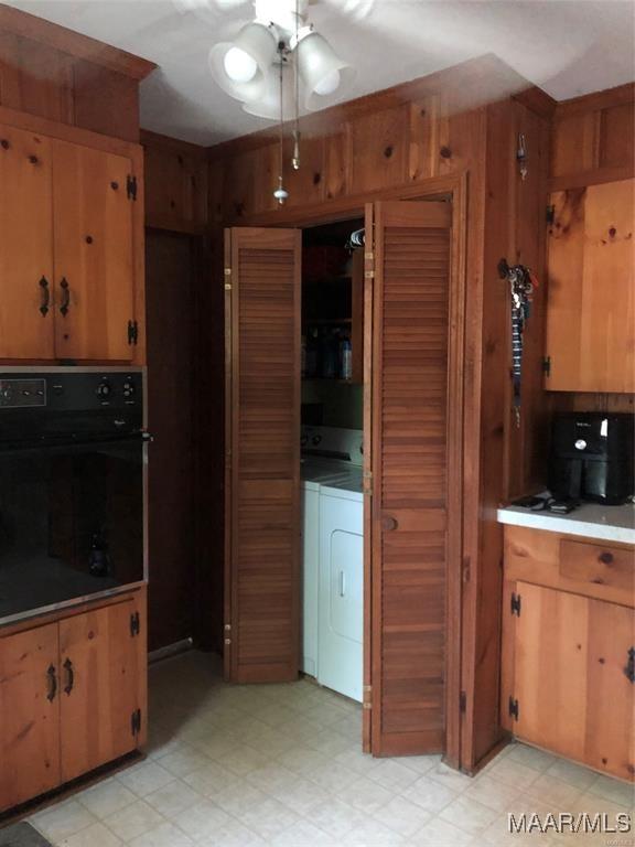 kitchen featuring black oven, ceiling fan, wooden walls, and washer and dryer