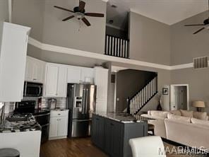 kitchen with black range with electric cooktop, dark hardwood / wood-style flooring, stainless steel fridge, a towering ceiling, and white cabinets