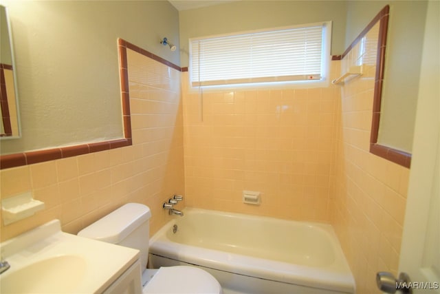 full bathroom featuring tiled shower / bath, vanity, toilet, and tile walls