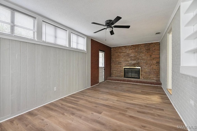 unfurnished living room with a textured ceiling, ceiling fan, wooden walls, wood-type flooring, and a stone fireplace