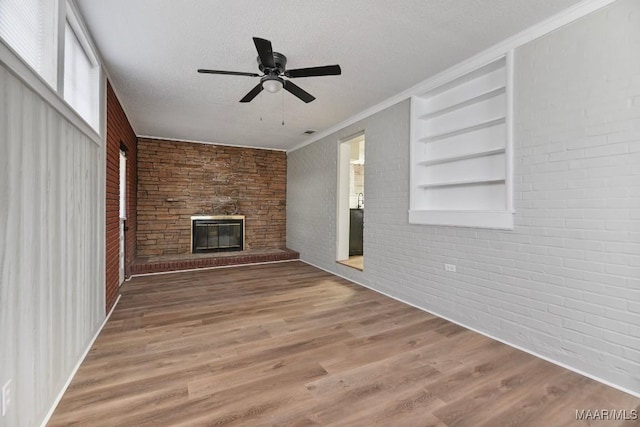 unfurnished living room featuring ceiling fan, built in features, a fireplace, wood-type flooring, and brick wall