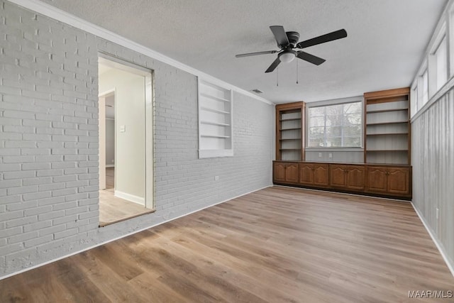 interior space featuring ceiling fan, brick wall, crown molding, light hardwood / wood-style floors, and a textured ceiling