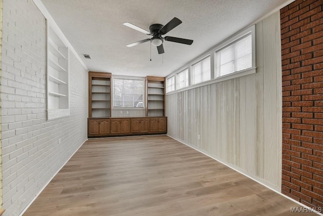 unfurnished living room with built in shelves, ceiling fan, brick wall, light hardwood / wood-style floors, and a textured ceiling