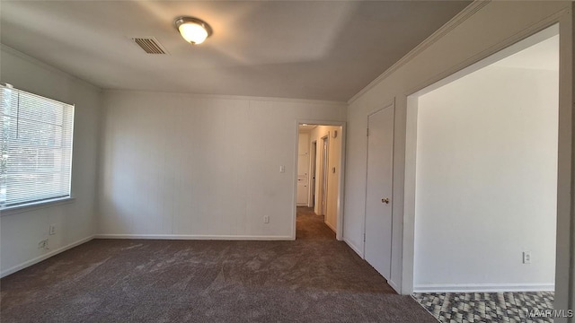 empty room featuring a wealth of natural light, dark carpet, and ornamental molding