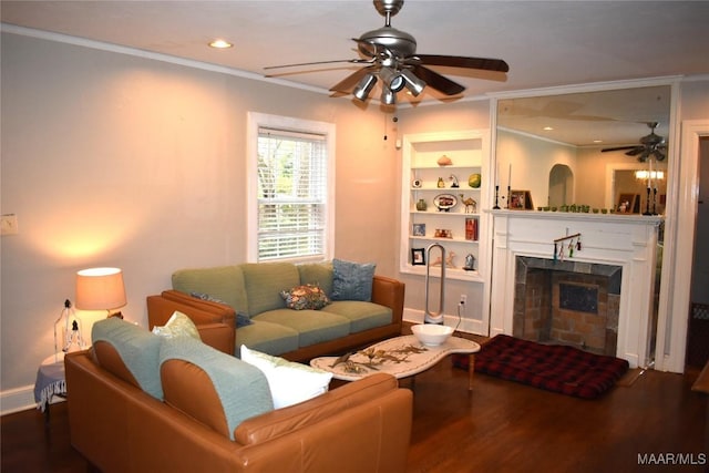 living room with built in shelves, ceiling fan, wood-type flooring, a fireplace, and ornamental molding