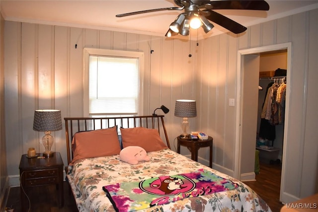 bedroom with dark wood-type flooring, a walk in closet, ceiling fan, ornamental molding, and a closet