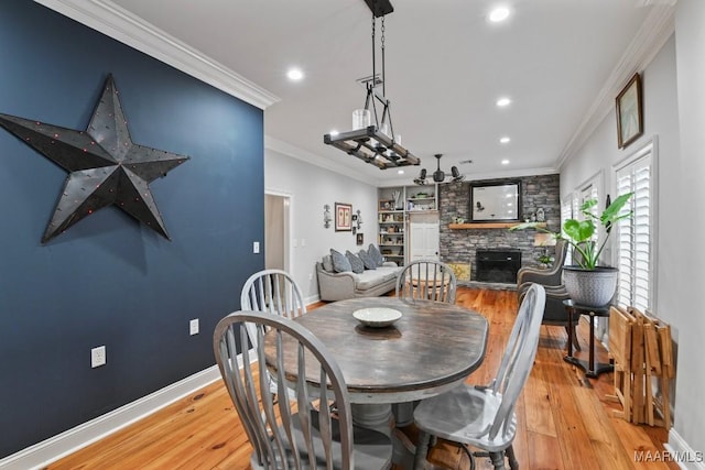 dining room featuring a fireplace, built in shelves, light hardwood / wood-style flooring, and crown molding