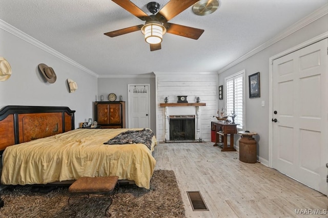 bedroom with a brick fireplace, a textured ceiling, ceiling fan, crown molding, and hardwood / wood-style floors